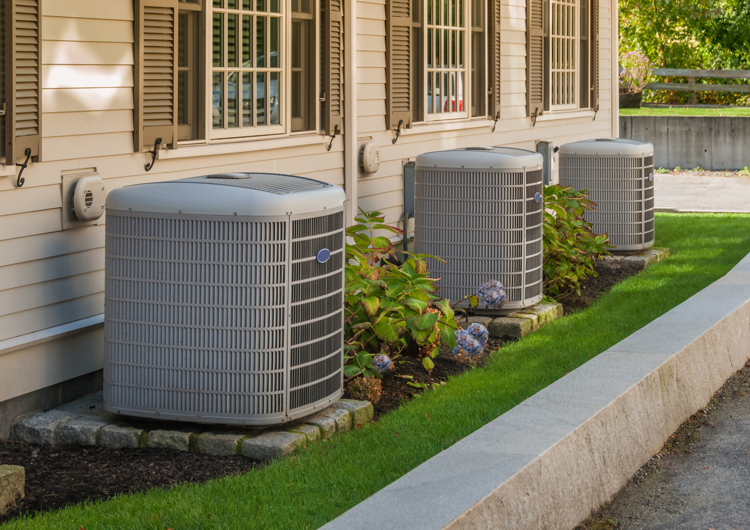 Three outdoor air conditioning units beside a home